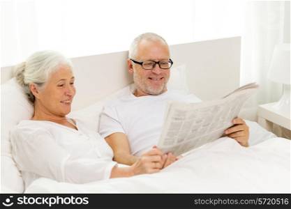 family, bedtime, resting, age and people concept - happy senior coupler with newspaper lying in bad at home