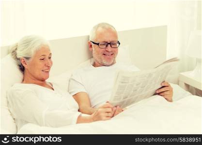 family, bedtime, resting, age and people concept - happy senior coupler with newspaper lying in bad at home