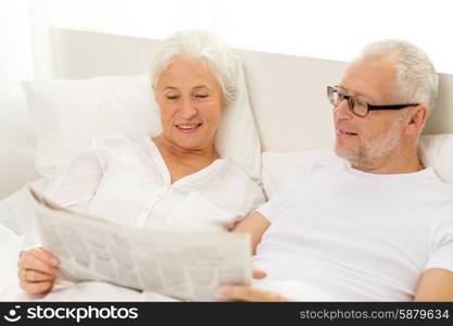 family, bedtime, resting, age and people concept - happy senior coupler with newspaper lying in bad at home