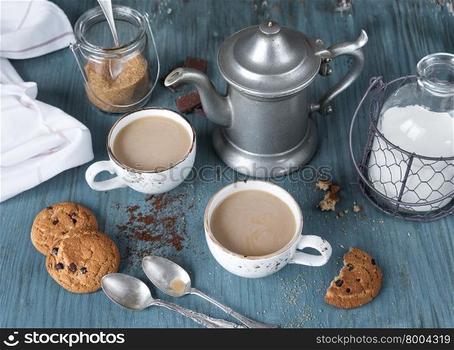 Family breakfast - two cups of coffee with milk espresso and homemade oatmeal cookies with chocolate on a blue wooden vintage table, rustic style, top view
