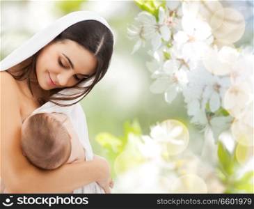 family, breastfeeding and motherhood concept - happy young mother with little baby sucking breast over cherry blossom background. mother breast feeding baby over cherry blossoms