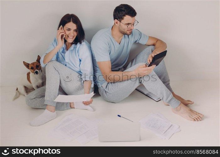 Family budget, payment, finances concept. Family couple analyze documents together, calculate expenses, use calculator, laptop computer, pose on floor, work from home, isolated over white background