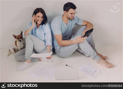 Family budget, payment, finances concept. Family couple analyze documents together, calculate expenses, use calculator, laptop computer, pose on floor, work from home, isolated over white background