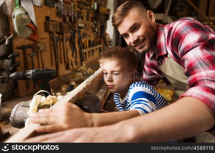 family, carpentry, woodwork and people concept - father and little son testing wood plank evenness at workshop