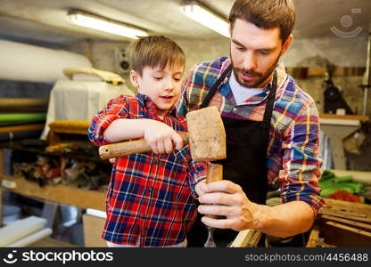 family, carpentry, woodwork and people concept - father and little son with hammer and chisel working with wood plank at workshop