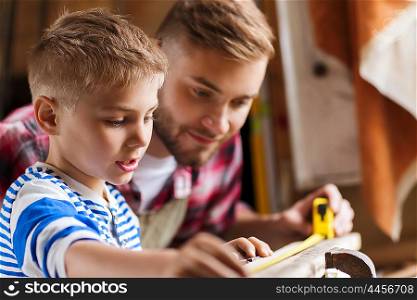 family, carpentry, woodwork and people concept - father and little son with ruler measuring wood plank at workshop