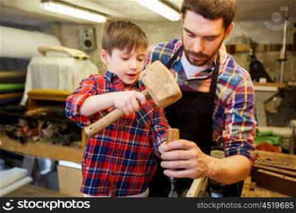 family, carpentry, woodwork and people concept - father and little son with hammer and chisel working with wood plank at workshop