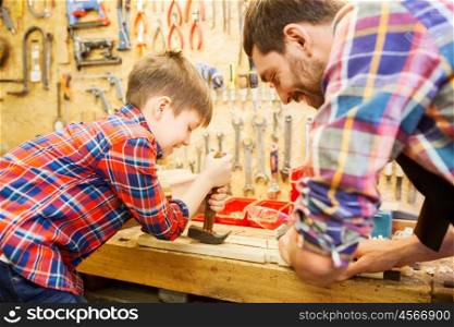 family, carpentry, woodwork and people concept - father and little son with claw hammer pulling nail out of wood plank at workshop