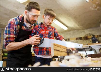 family, carpentry, woodwork and people concept - father and little son with saw sawing wood plank at workshop