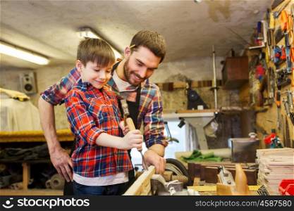 family, carpentry, woodwork and people concept - father and little son with hammer and chisel working with wood plank at workshop