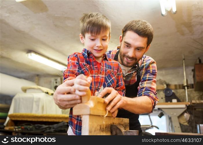 family, carpentry, woodwork and people concept - father and little son with plane working with wood plank at workshop