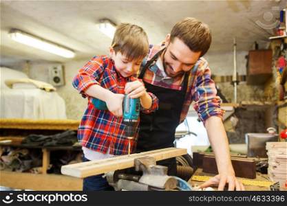 family, carpentry, woodwork and people concept - father and little son with drill perforating wood plank at workshop