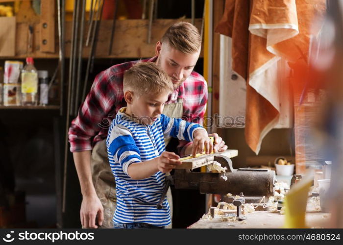 family, carpentry, woodwork and people concept - father and little son with ruler and pencil measuring wood plank at workshop