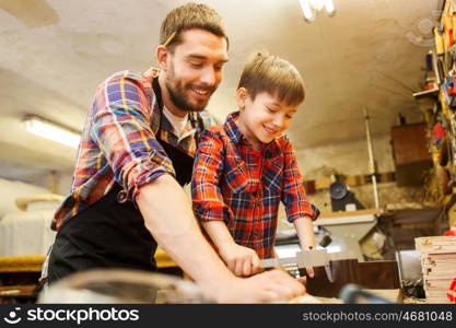 family, carpentry, woodwork and people concept - father and little son with calipers measuring wood plank at workshop