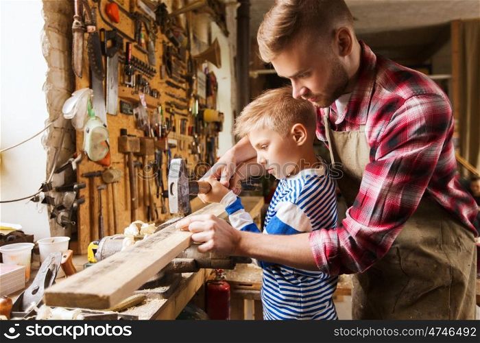 family, carpentry, woodwork and people concept - father and little son with hammer hammering nail into wood plank at workshop