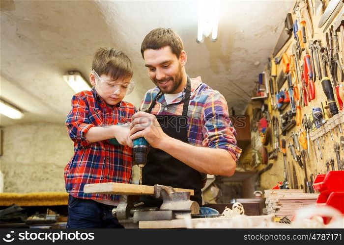 family, carpentry, woodwork and people concept - father and little son with drill perforating wood plank at workshop