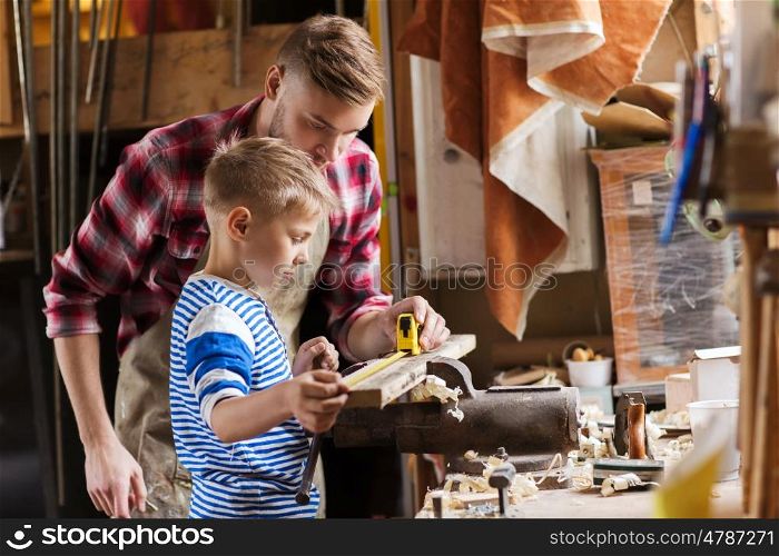 family, carpentry, woodwork and people concept - father and little son with ruler and pencil measuring wood plank at workshop