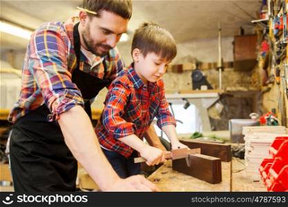 family, carpentry, woodwork and people concept - father and little son with calipers measuring wood plank at workshop