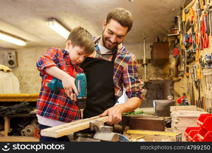 family, carpentry, woodwork and people concept - father and little son with drill perforating wood plank at workshop