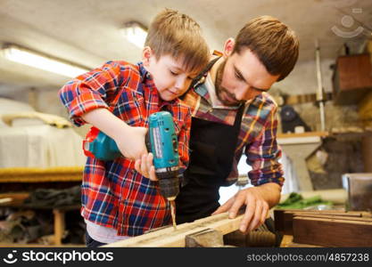 family, carpentry, woodwork and people concept - father and little son with drill perforating wood plank at workshop