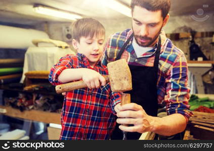 family, carpentry, woodwork and people concept - father and little son with hammer and chisel working with wood plank at workshop. father and son with chisel working at workshop. father and son with chisel working at workshop