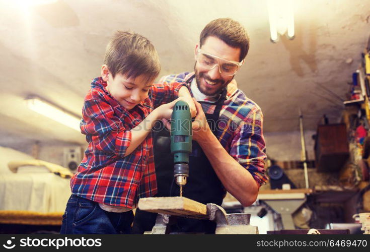 family, carpentry, woodwork and people concept - father and little son with drill perforating wood plank at workshop. father and son with drill working at workshop