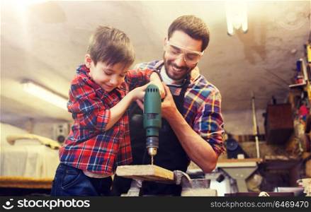 family, carpentry, woodwork and people concept - father and little son with drill perforating wood plank at workshop. father and son with drill working at workshop