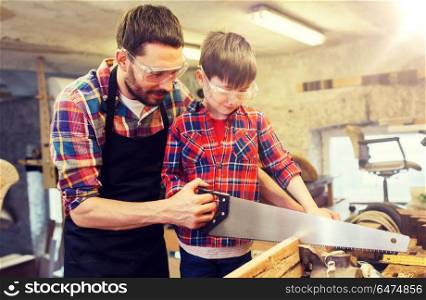 family, carpentry, woodwork and people concept - father and little son with saw sawing wood plank at workshop. father and son with saw working at workshop. father and son with saw working at workshop