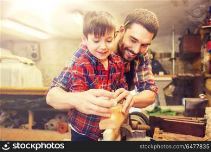 family, carpentry, woodwork and people concept - father and little son with plane working with wood plank at workshop. father and son with plane shaving wood at workshop. father and son with plane shaving wood at workshop