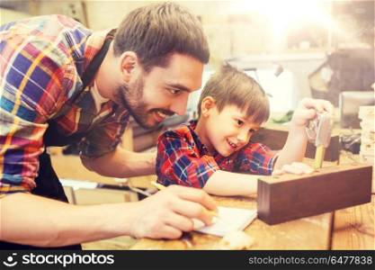 family, carpentry, woodwork and people concept - father and little son with ruler and pencil measuring wood plank and writing dimensions to notebook at workshop. dad and son with ruler measuring plank at workshop. dad and son with ruler measuring plank at workshop