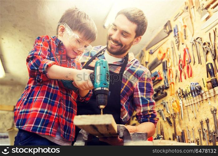 family, carpentry, woodwork and people concept - father and little son with drill perforating wood plank at workshop. father and son with drill working at workshop. father and son with drill working at workshop