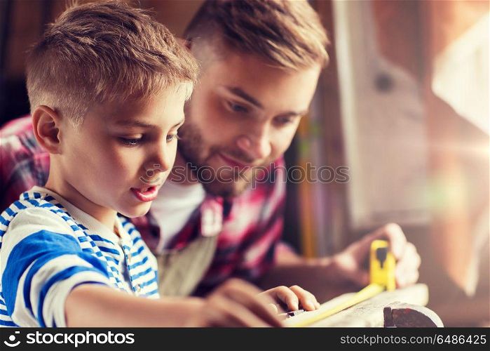 family, carpentry, woodwork and people concept - father and little son with ruler measuring wood plank at workshop. father and son with ruler measure wood at workshop. father and son with ruler measure wood at workshop