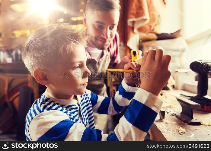 family, carpentry, woodwork and people concept - father and little son with ruler and pencil measuring wood plank at workshop. father and son with ruler measure wood at workshop. father and son with ruler measure wood at workshop