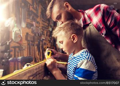 family, carpentry, woodwork and people concept - father and little son with ruler and pencil measuring wood plank at workshop. father and son with ruler measure wood at workshop. father and son with ruler measure wood at workshop