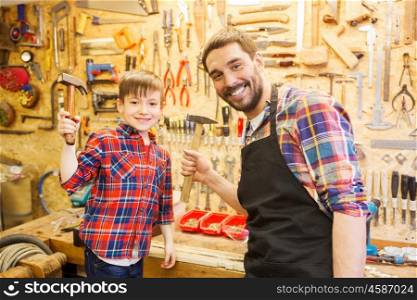 family, carpentry, woodwork and people concept - father and little son with hammers at workshop