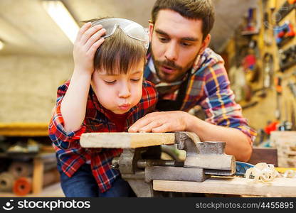 family, carpentry, woodwork and people concept - father and little son working with wood plank at workshop