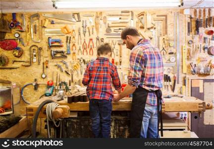 family, carpentry, woodwork and people concept - father and little son working with wood plank at workshop