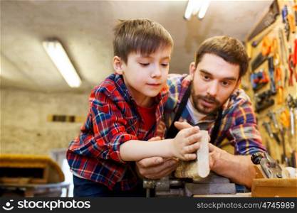 family, carpentry, woodwork and people concept - father and little son working with wood plank at workshop