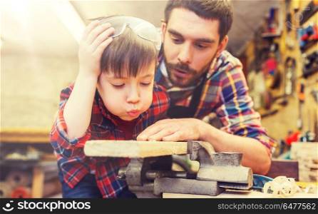 family, carpentry, woodwork and people concept - father and little son working with wood plank at workshop. father and little son with wood plank at workshop. father and little son with wood plank at workshop