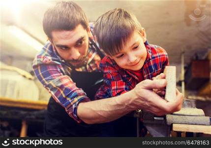 family, carpentry, woodwork and people concept - father and little son working with wood plank at workshop. father and little son with wood plank at workshop. father and little son with wood plank at workshop