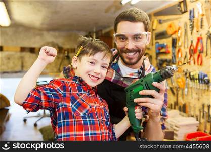 family, carpentry, woodwork and people concept - happy father and little son with drill working at workshop