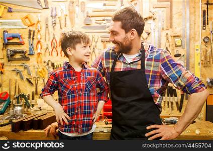family, carpentry, woodwork and people concept - happy father and little son working with work tools and wood planks at workshop