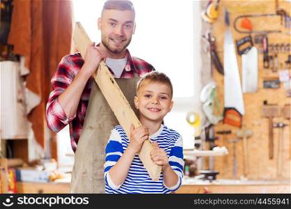 family, carpentry, woodwork and people concept - happy father and little son carrying wood plank at workshop