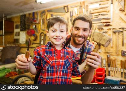 family, carpentry, woodwork and people concept - happy father and little son with hammer and chisel working at workshop