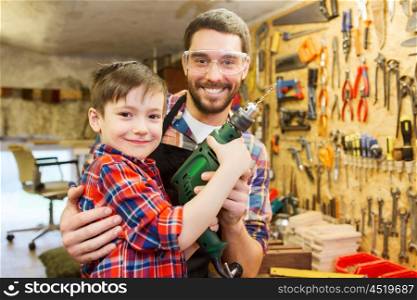 family, carpentry, woodwork and people concept - happy father and little son with drill working at workshop