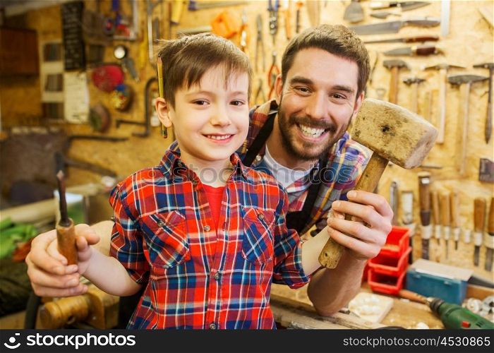 family, carpentry, woodwork and people concept - happy father and little son with hammer and chisel working at workshop