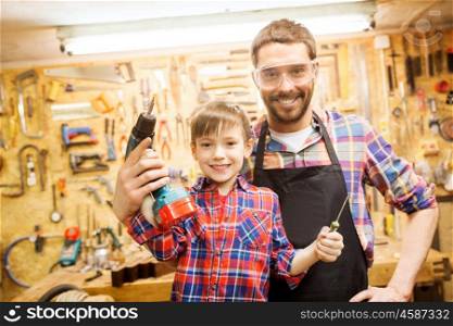 family, carpentry, woodwork and people concept - happy father and little son with drill and screwdriver working at workshop