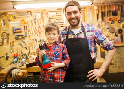 family, carpentry, woodwork and people concept - happy father and little son with drill working at workshop