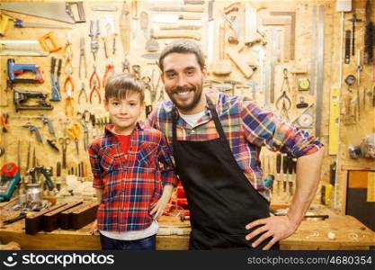 family, carpentry, woodwork and people concept - happy father and little son working with work tools and wood planks at workshop