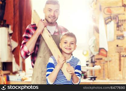 family, carpentry, woodwork and people concept - happy father and little son carrying wood plank at workshop. happy father and son with wood plank at workshop. happy father and son with wood plank at workshop